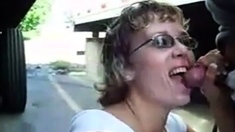 Mature woman sucks cock between trucks in parking lot